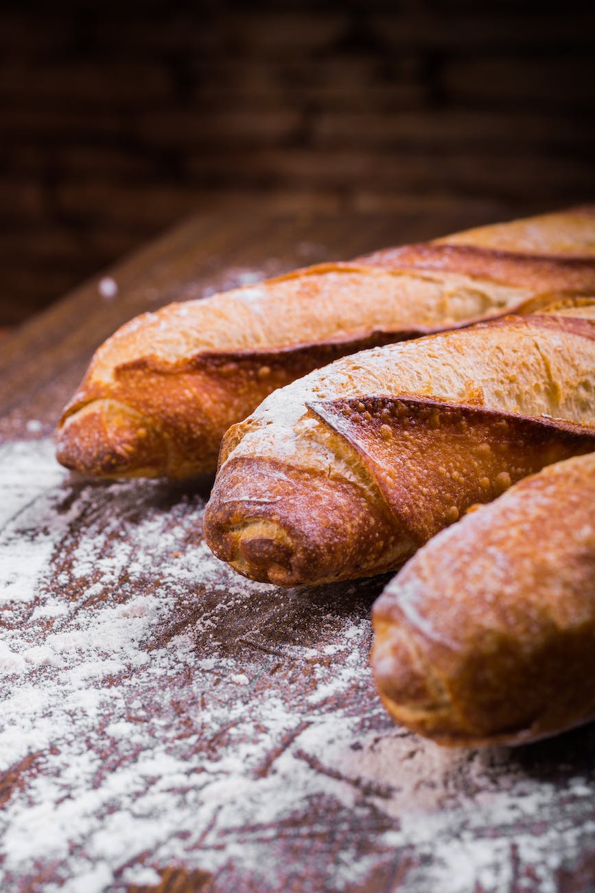 close up photo of three baguettes on brown wooden surface with white powder